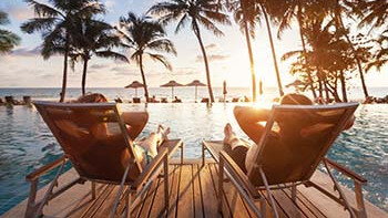Zwei Personen sitzen am Pool mit Palmen im Hintergrund