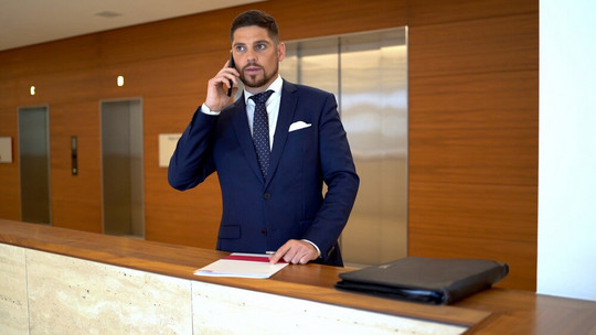 Makler steht vor einem Lift und telefoniert in einem Gebäude