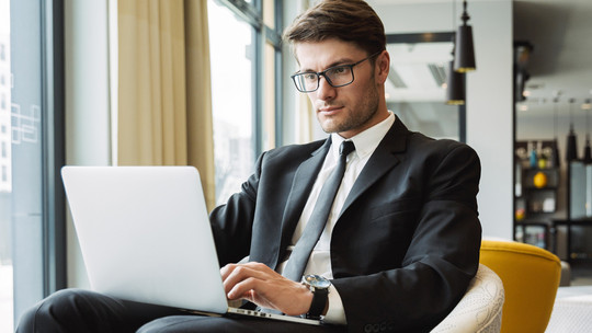 Un homme en complet est assis dans un café, devant un ordinateur portable