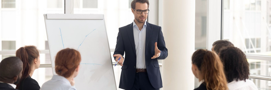 Mann steht an einem Flipchart und hält mit sechs weiteren Personen eine Sitzung ab