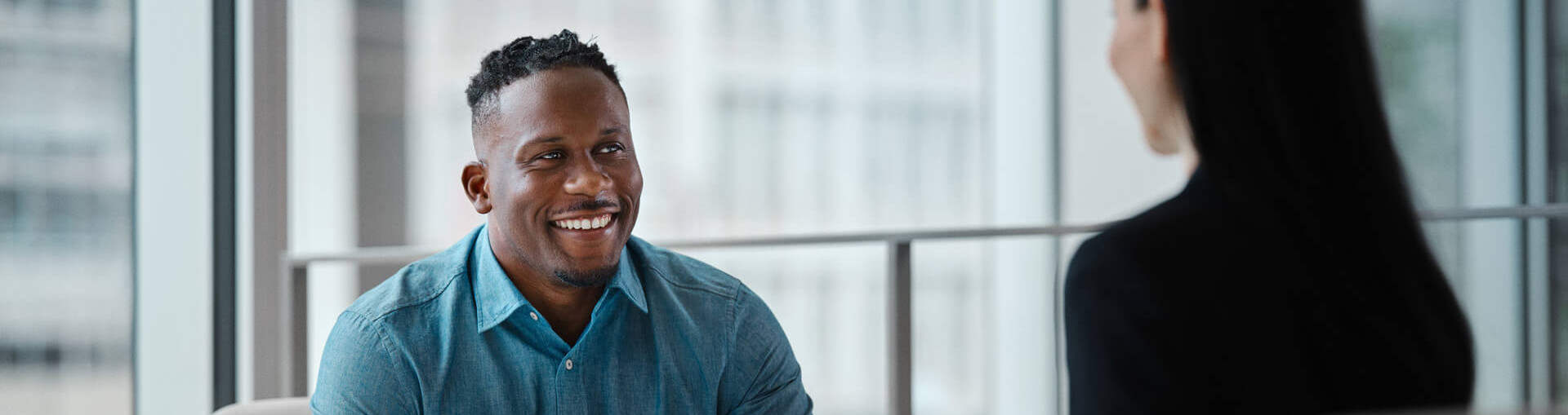 Gros plan sur un homme souriant, qui regarde la courtière assise en face de lui