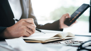 Une personne en costume fait des calculs au bureau avec une calculatrice et tient un stylo à la main.