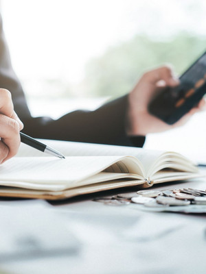 Person im Anzug rechnet im Büro mit dem Taschenrechner und hält einen Stift in der Hand