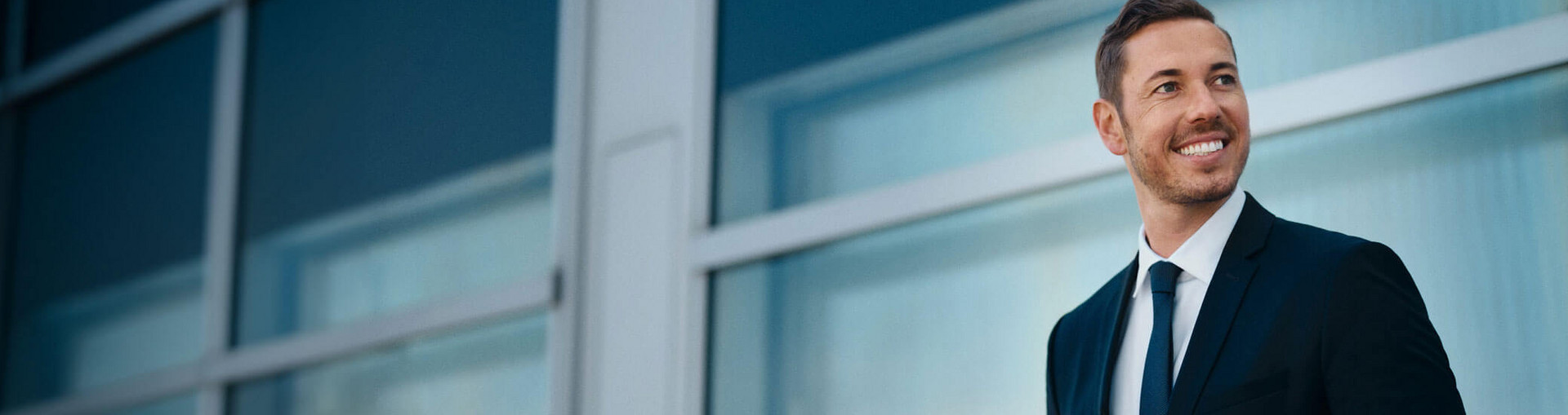 Makler steht vor einer Glasscheibe und schaut in die Ferne
