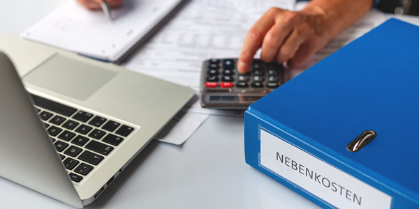 Mann tippt auf Taschenrechner neben Ordner mit Nebenkosten
