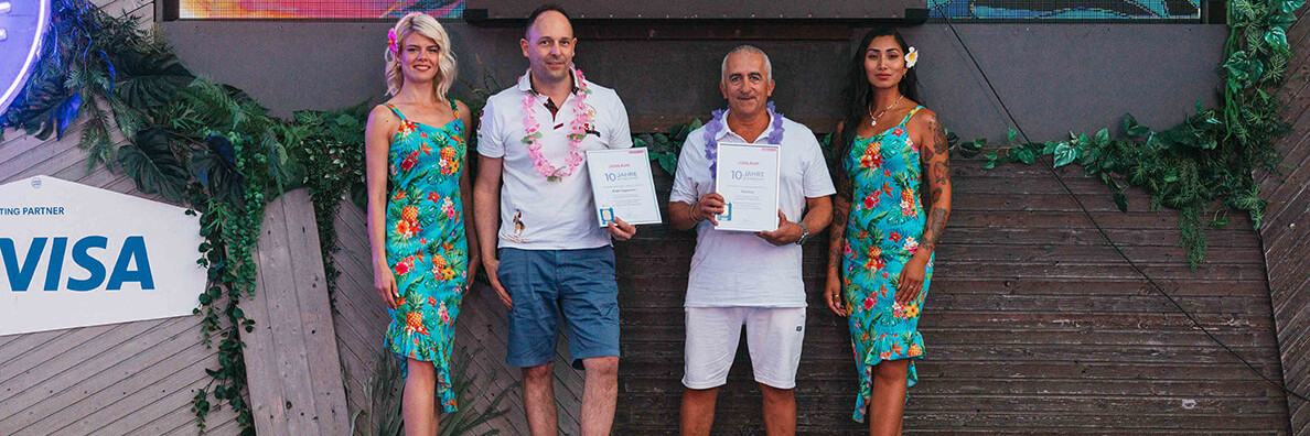 Männer halten Urkunde auf Foto mit Hostessen im Hawaii Kleid