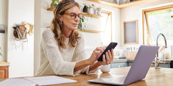 Frau an Handy mit Laptop und Dokumenten