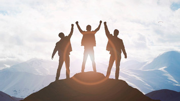 Trois hommes se tiennent sur un sommet et tendent les mains vers le haut