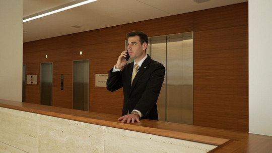 Makler steht vor einem Lift und telefoniert in einem Gebäude